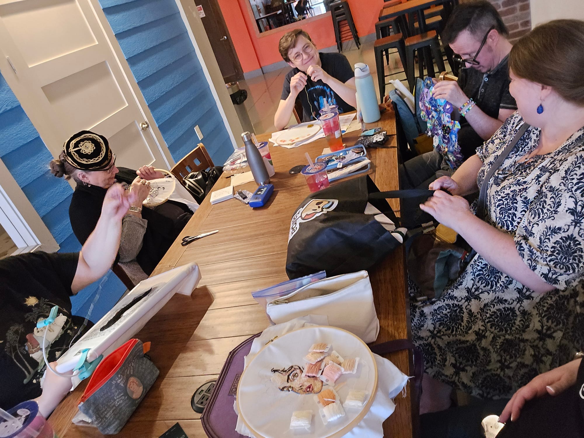 Live at a Creativity Social in Houston - several individuals sit around a cafe table, one with a bag and the others working on embroidery and sewing projects.